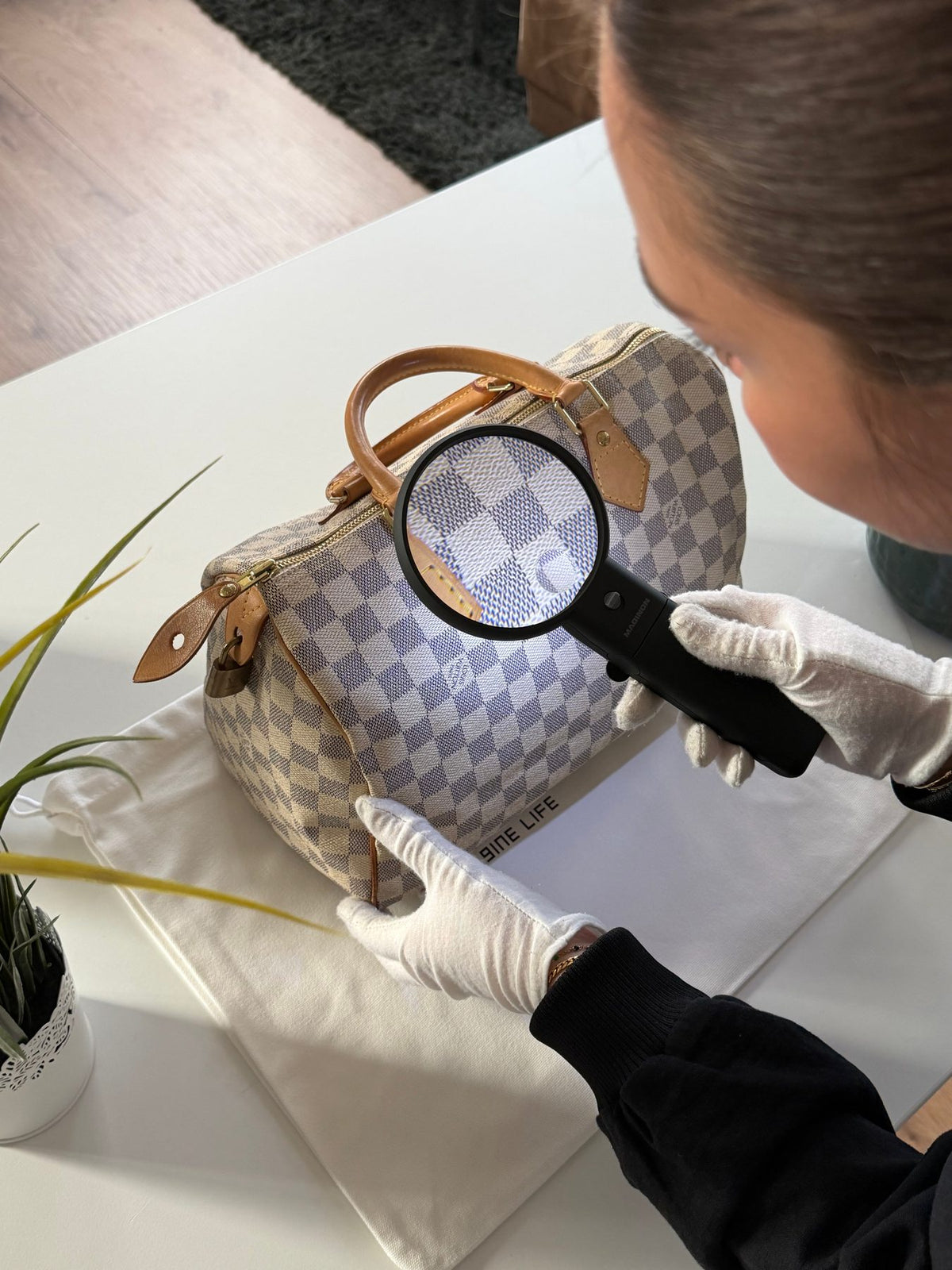 Echtheitsprüfung einer Louis Vuitton Speedy Damier Azur mit Lupe und weißen Handschuhen